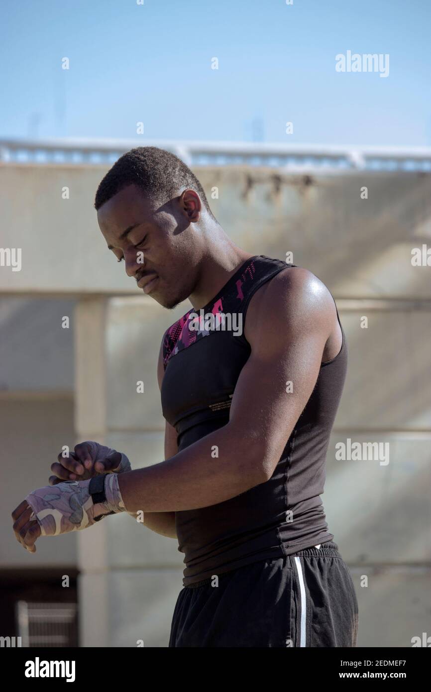 Il giovane pugile nero professionista in t-shirt nera gli bende le mani Pronto per il box durante il Covid 19 pandemic Outdoors.Boxing e. Concetto di formazione 2021 Foto Stock