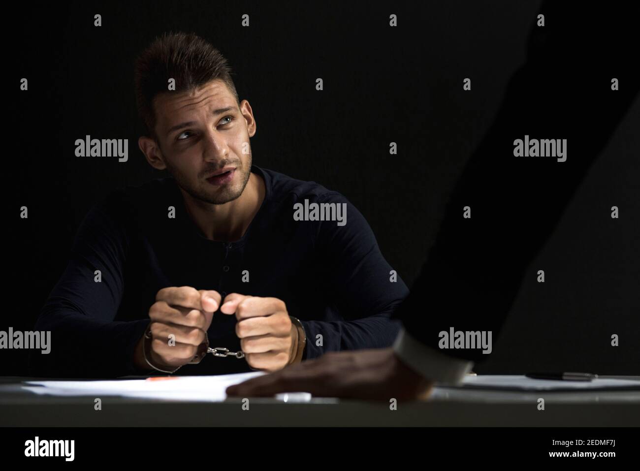 Uomo sospetto o criminale con manette intervistate dall'ufficiale nella sala degli interrogatori Foto Stock