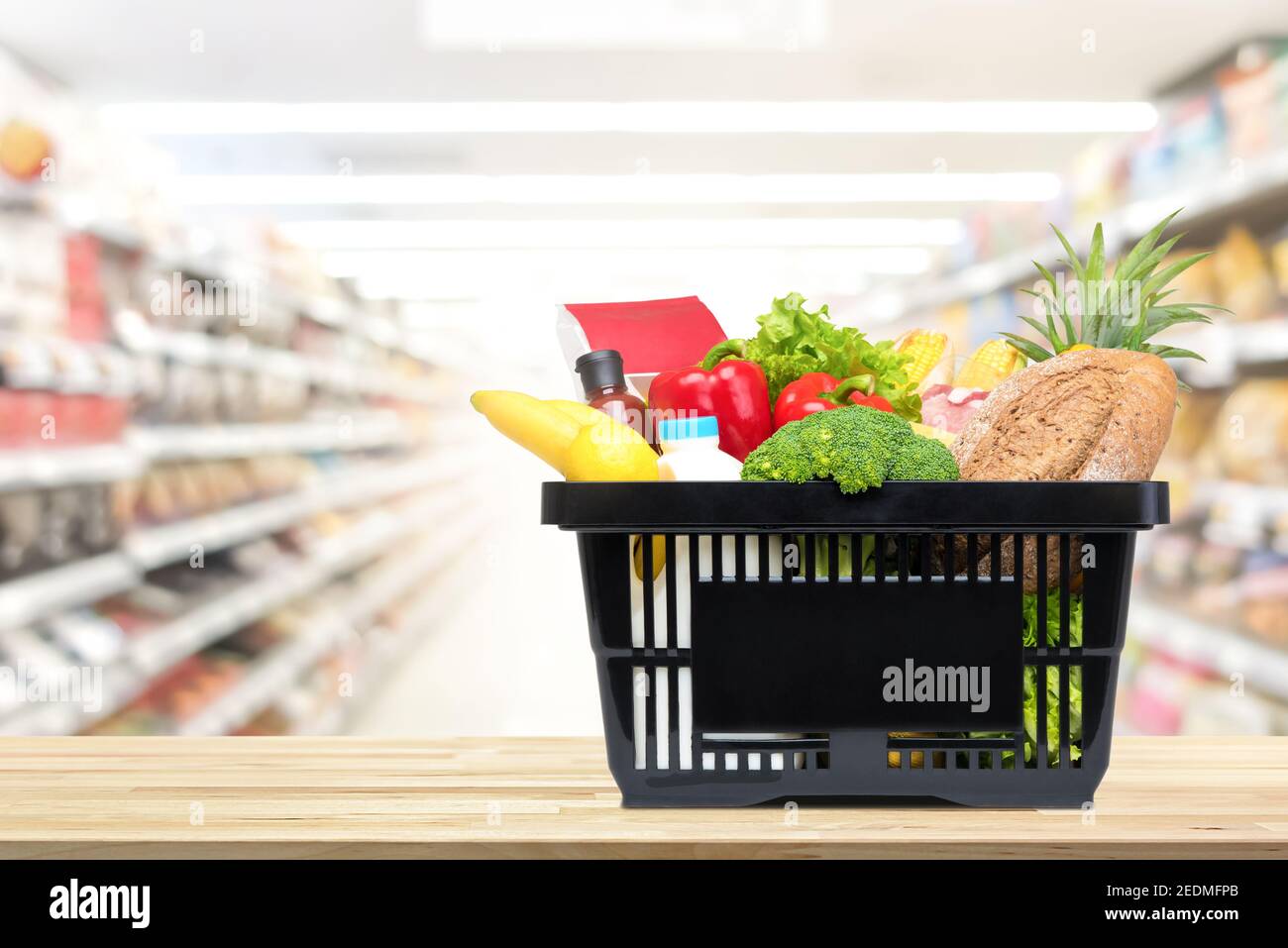 Cibo e generi alimentari nel cestino della spesa su tavola di legno con corridoio del mercato supermarket sfocato in background Foto Stock