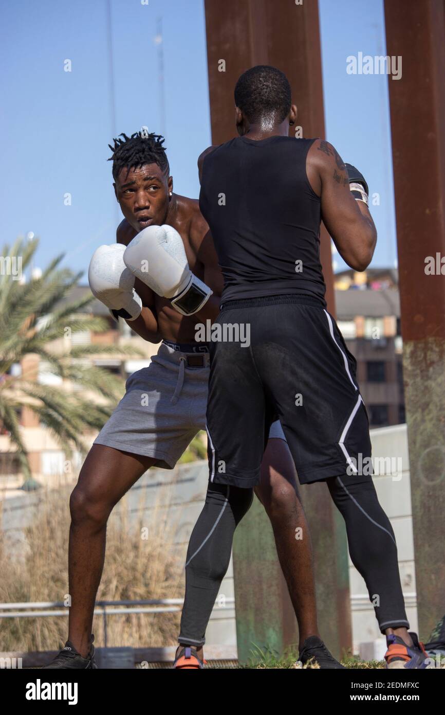 Il pugile nero professionista allena il principiante nero del boxer con i guanti di boxing una classe di boxing all'aperto in una giornata soleggiata mentre entrambi sudano. Concetto di boxe. Foto Stock