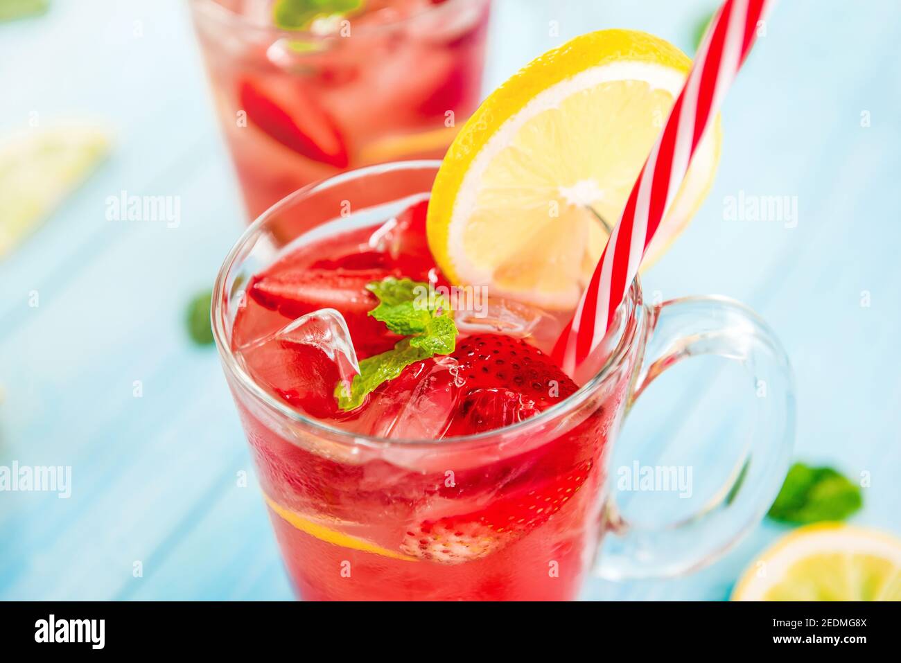 Bevande rinfrescanti e colorate per l'estate, dolce freddo e succo di limonata di fragole acesate con cubetti di ghiaccio nei bicchieri guarniti con limoni a fette Foto Stock