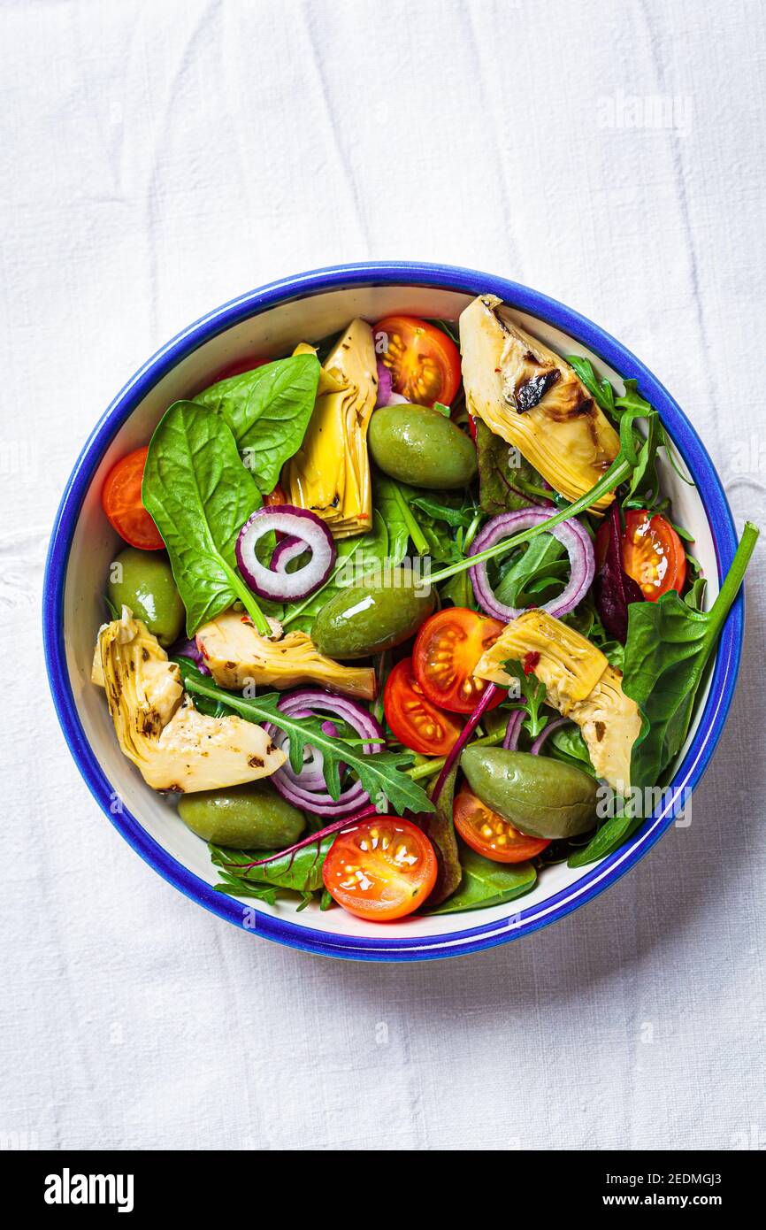 Insalata verde con carciofi, pomodori e olive in una ciotola bianca. Foto Stock