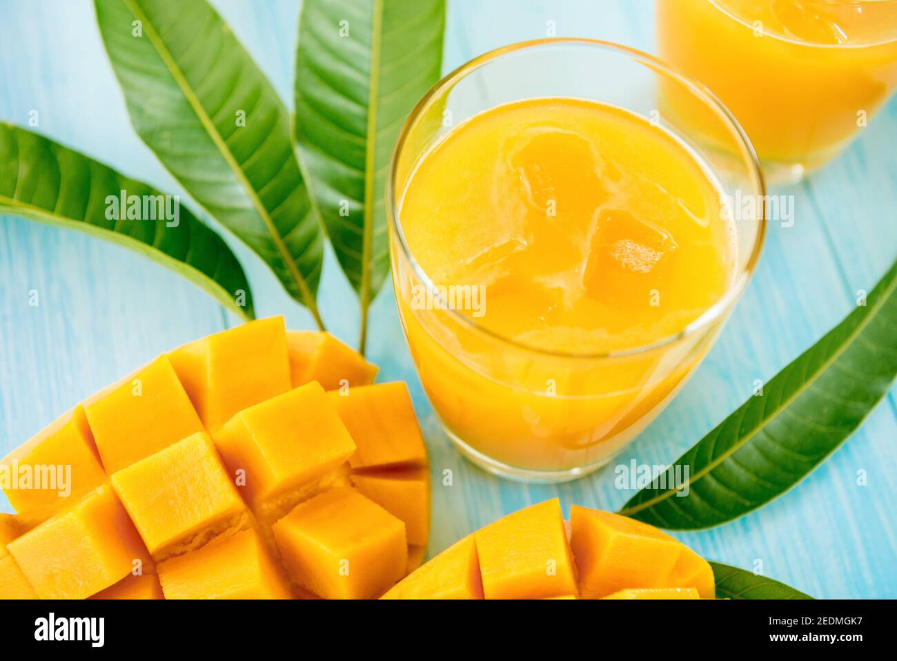 Bevande rinfrescanti per l'estate, dolce freddo e sour succo esotico di mango con cubetti di ghiaccio nei bicchieri su tavolo di legno blu chiaro Foto Stock