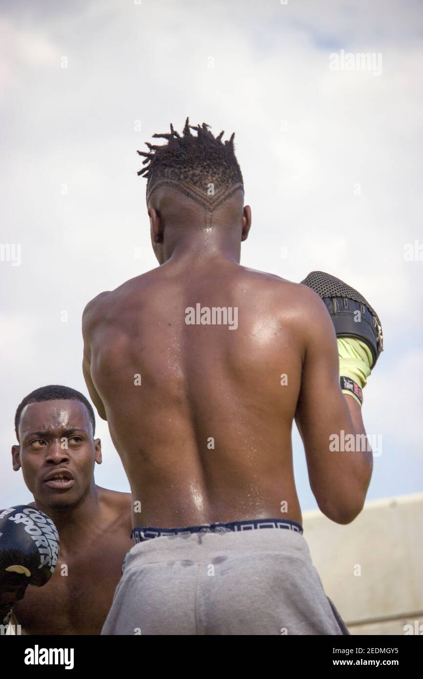 Il pugile nero professionista allena il principiante nero del boxer con i guanti di boxing una classe di boxing all'aperto in una giornata soleggiata mentre entrambi sudano. Concetto di boxe Foto Stock