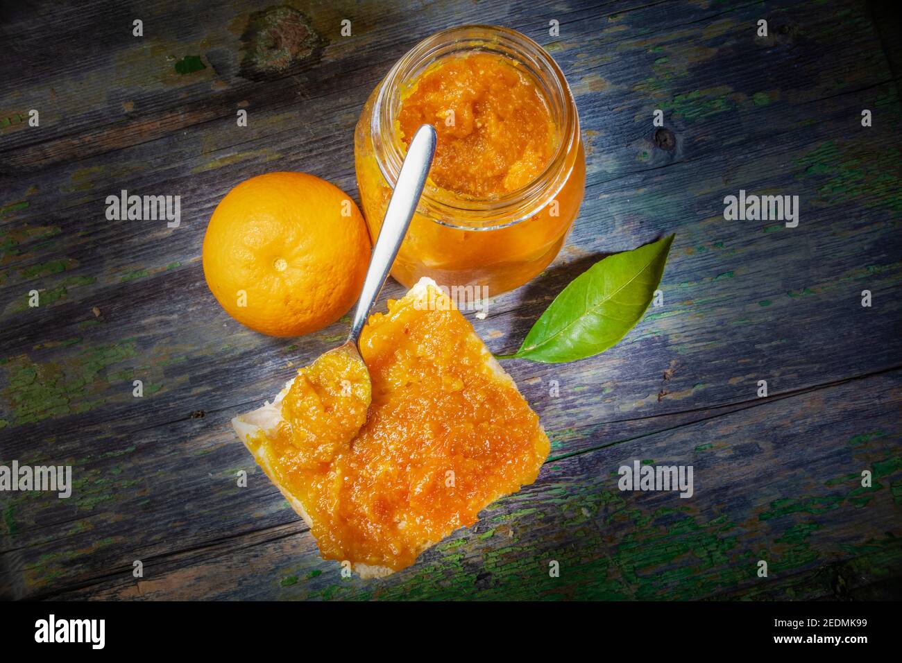 Marmellata d'arancia fresca pura con cucchiaio inclinato su pane spalmato con lenza d'arancia come ornamento. Copia spazio su entrambi i lati Foto Stock