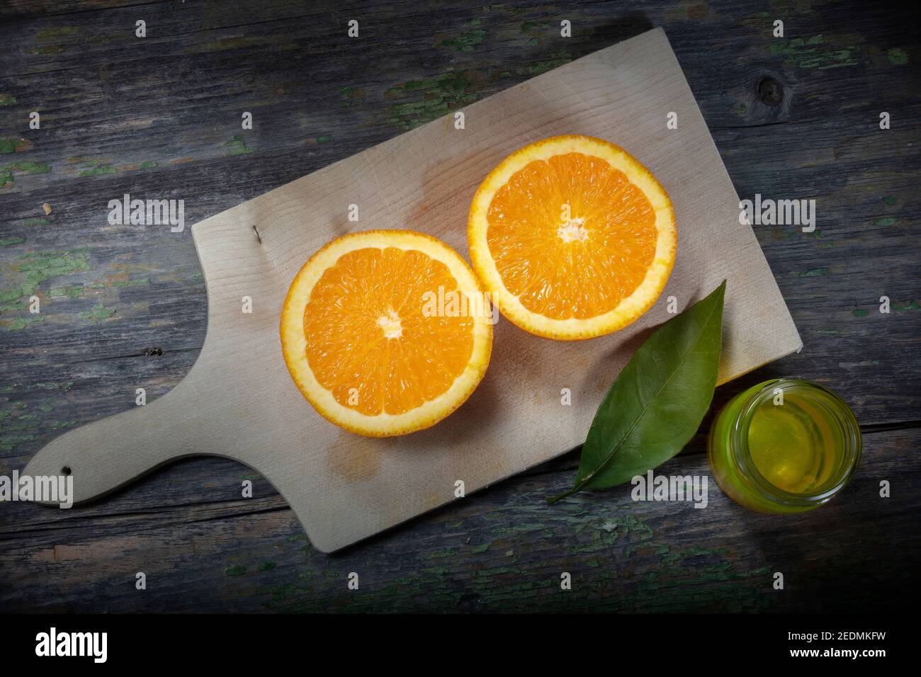 Foto macro di Still Life. ​​Oranges a metà fette su un tagliere. Vasetto piccolo di olio d'oliva e di arancia lasciare come decorazione Foto Stock