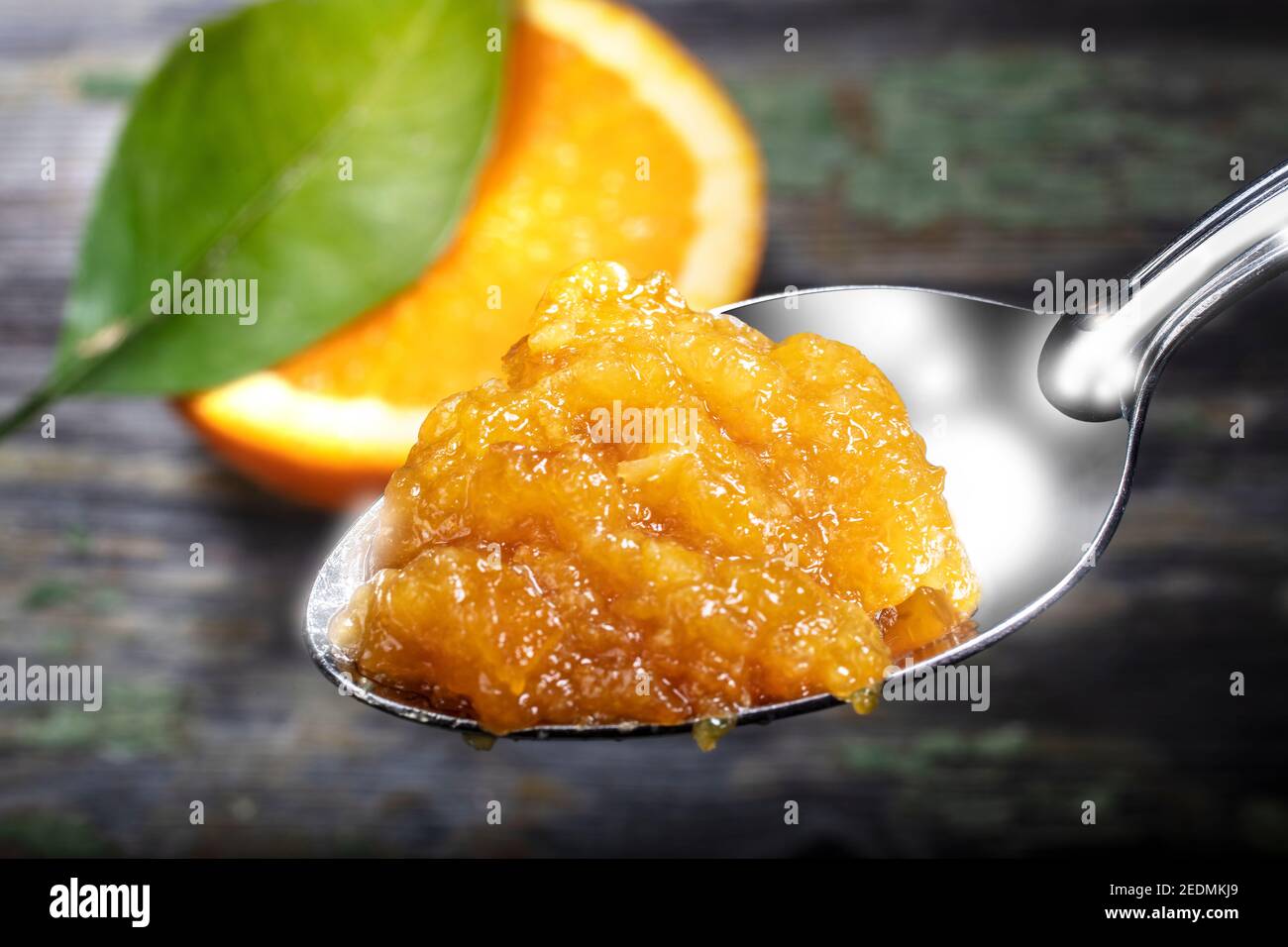 Fuoco selettivo sul cucchiaio di marmellata arancione.legno di sfondo è decorato con la fetta e il congedo di arancia. Foto Stock