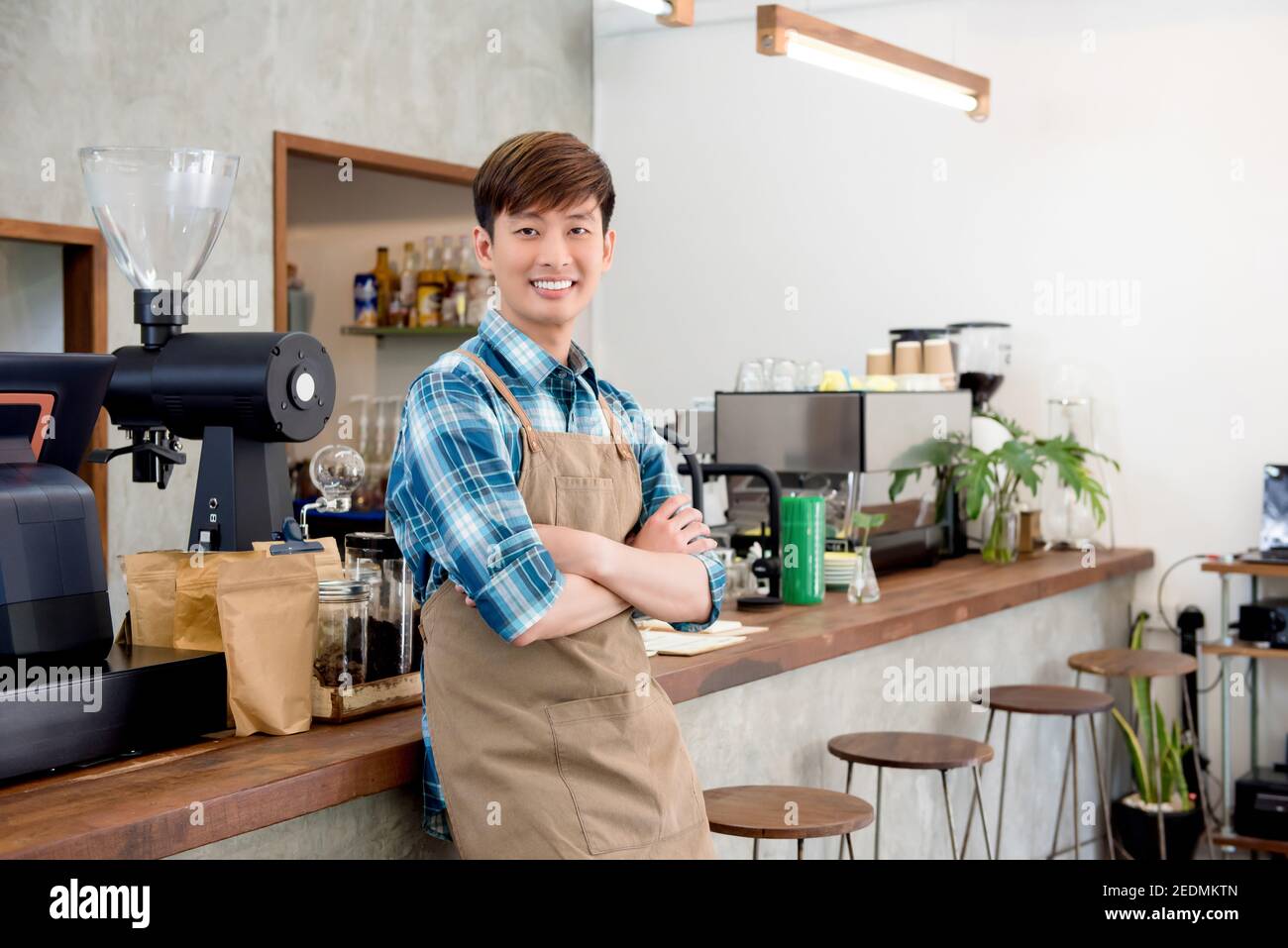 Allegro giovane imprenditore asiatico uomo in piedi con braccio attraversato a. bancone nella sua caffetteria Foto Stock