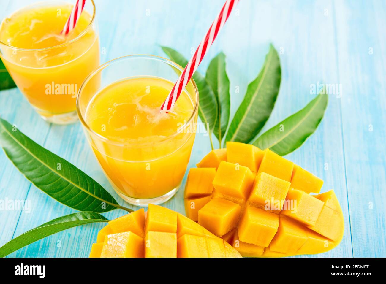 Bevande rinfrescanti per l'estate, dolce freddo e sour esotico succo di mango tropicale con cubetti di ghiaccio nei bicchieri su tavolo di legno blu chiaro Foto Stock