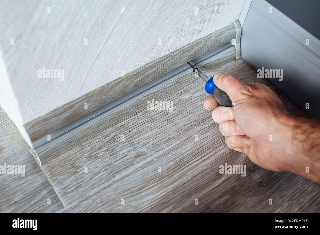 Il master monta un battiscopa in plastica sul laminato - fissaggio con viti alla parete - riparazione domestica Foto Stock