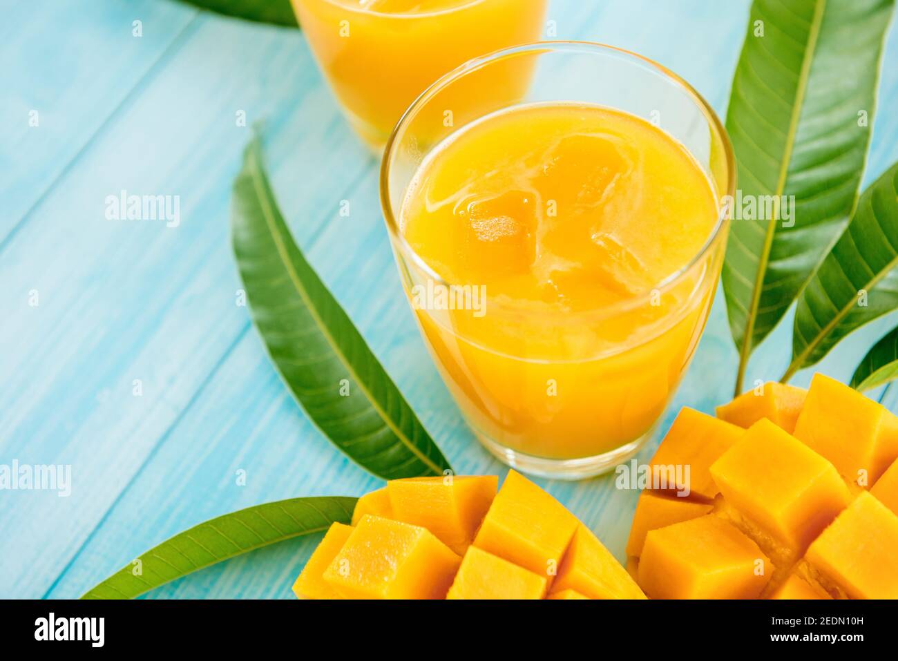 Bevande rinfrescanti per l'estate, dolce freddo e sour succo esotico di mango con cubetti di ghiaccio nei bicchieri su tavolo di legno blu chiaro Foto Stock