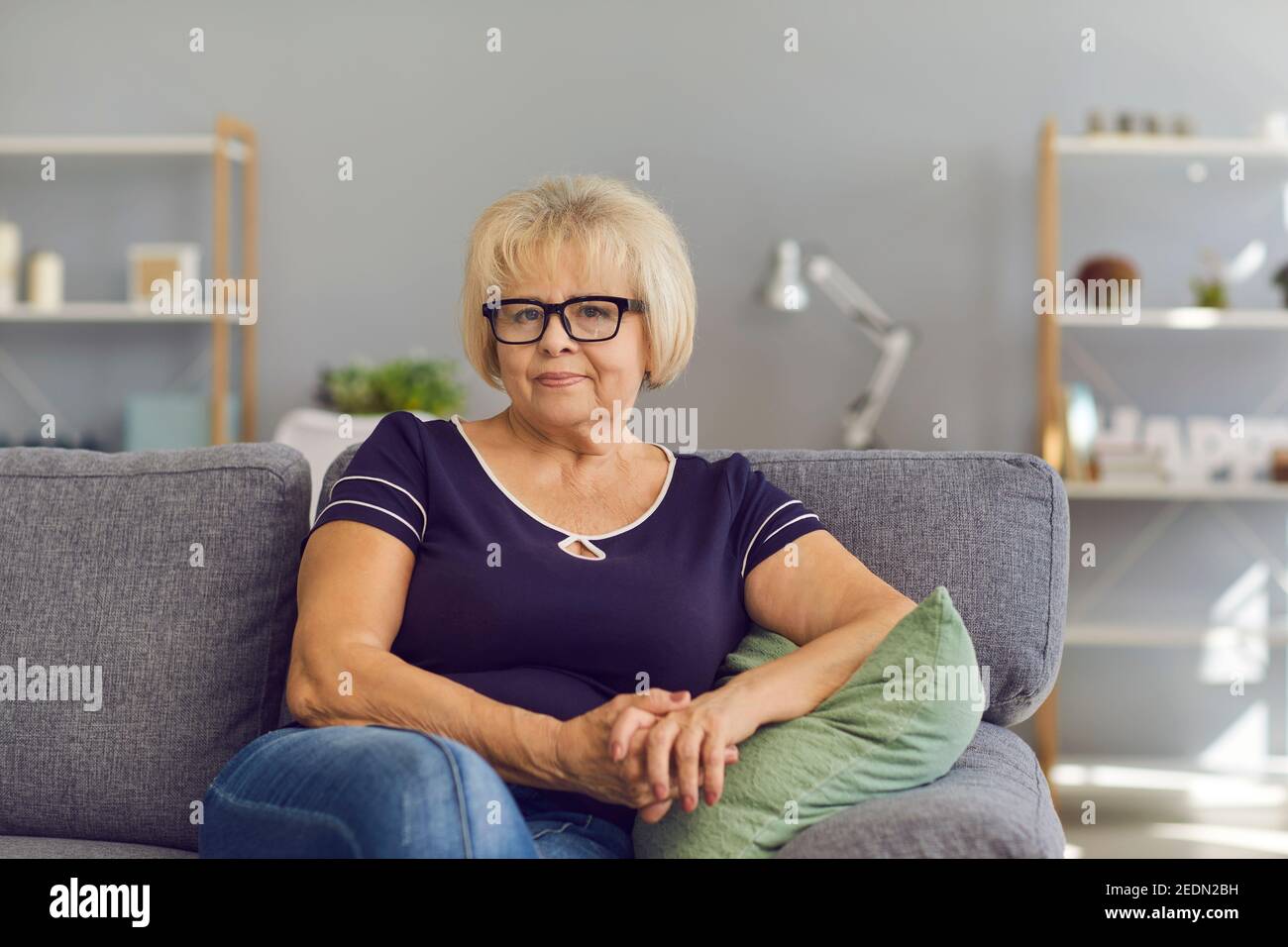 Donna anziana positiva nonna pensionato seduta sul divano a casa e guardando la fotocamera Foto Stock