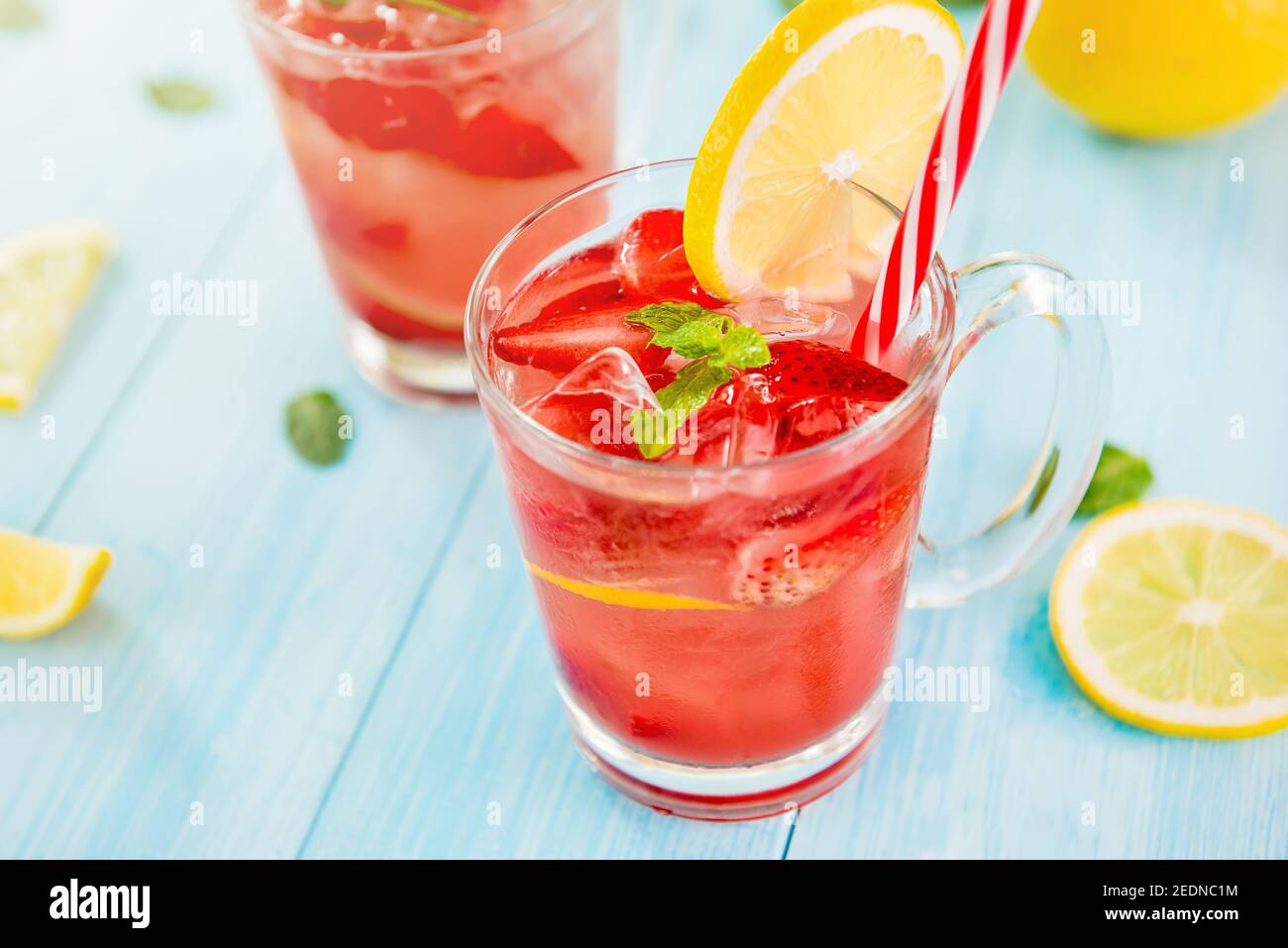Bevande rinfrescanti e colorate per l'estate, dolce freddo e succo di limonata di fragole con cubetti di ghiaccio nei bicchieri guarniti con limone a fette Foto Stock