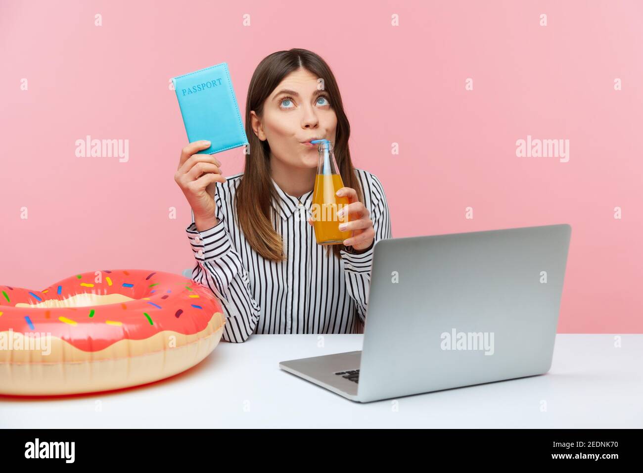Sognante donna pensabile bere limonata tenendo in mano il passaporto, immaginando vacanze all'estero seduto sul posto di lavoro con laptop e rin di gomma Foto Stock