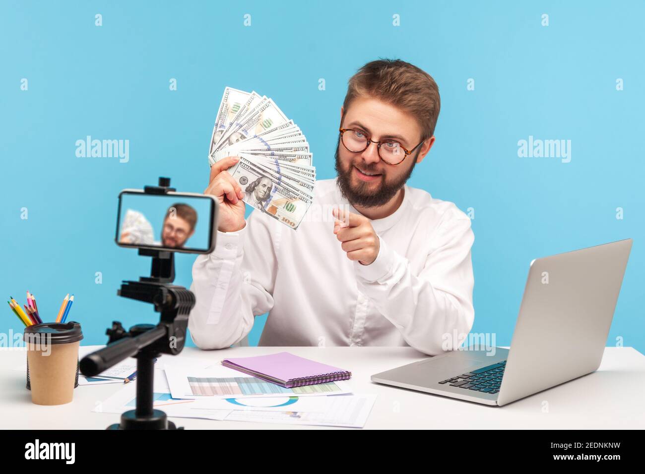 Sorridente uomo bearded vita allenatore tenendo fan di dollari e puntando il dito su di voi, registrare video sulla fotocamera smartphone, insegnare alfabetizzazione finanziaria. IO Foto Stock