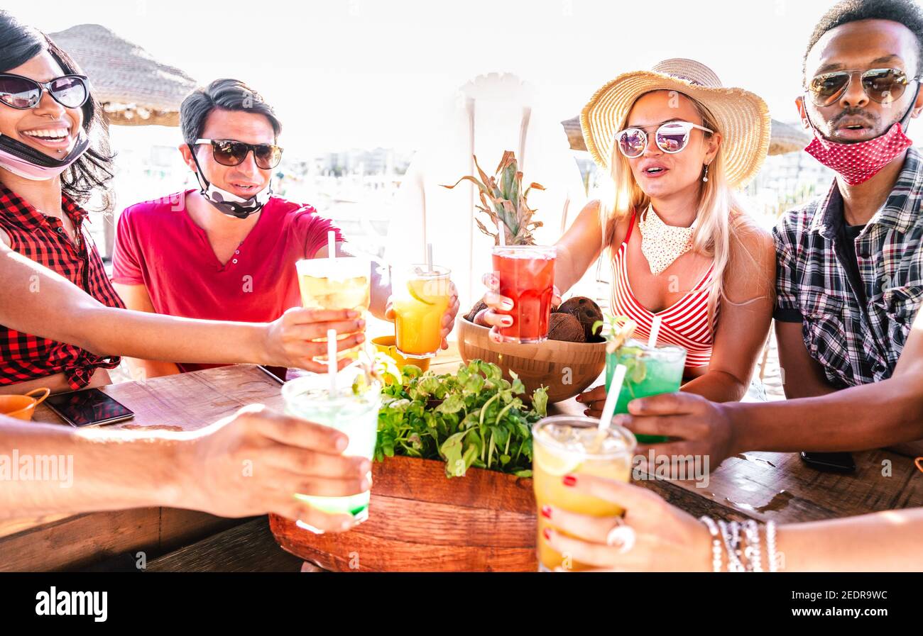 Giovani multiculturali che tostano al cocktail bar sulla spiaggia con aperto Maschera facciale - nuovo concetto estivo normale con milleniali avere divertimento insieme Foto Stock