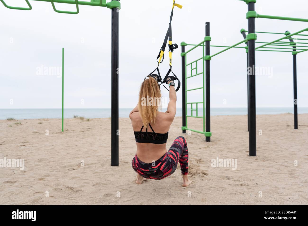 Giovane donna atletica fitness che si esercita facendo allenamento sospensione con trx Cinghie fitness su bar all'aperto spiaggia gym.Crossfit allenamento, body building , s Foto Stock