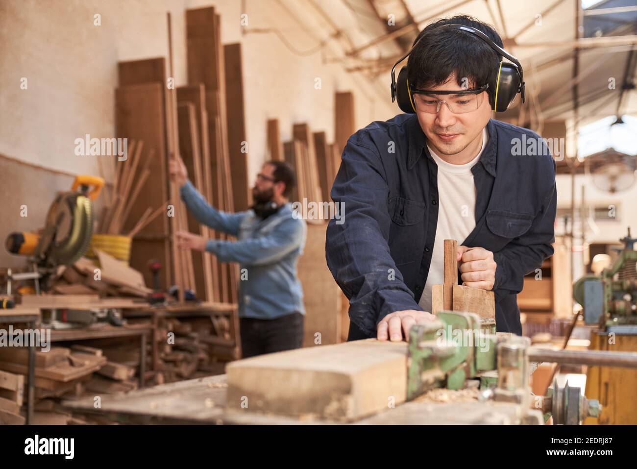 Giovane uomo come apprendista artigiano al pianificatore in la falegnameria Foto Stock