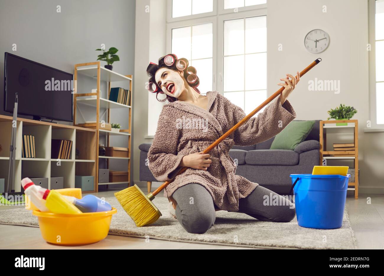 Housewife felice divertirsi, suonare su una chitarra polizietta e cantare mentre si sta riassestando a casa Foto Stock