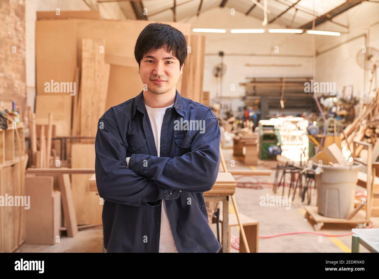 Giovane uomo con le braccia ripiegate come apprendista nel officina di falegnameria Foto Stock