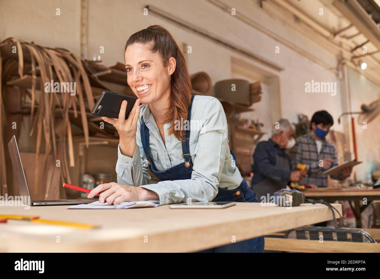 Donna artigiana al telefono che parla con un cliente l'officina di falegnameria Foto Stock