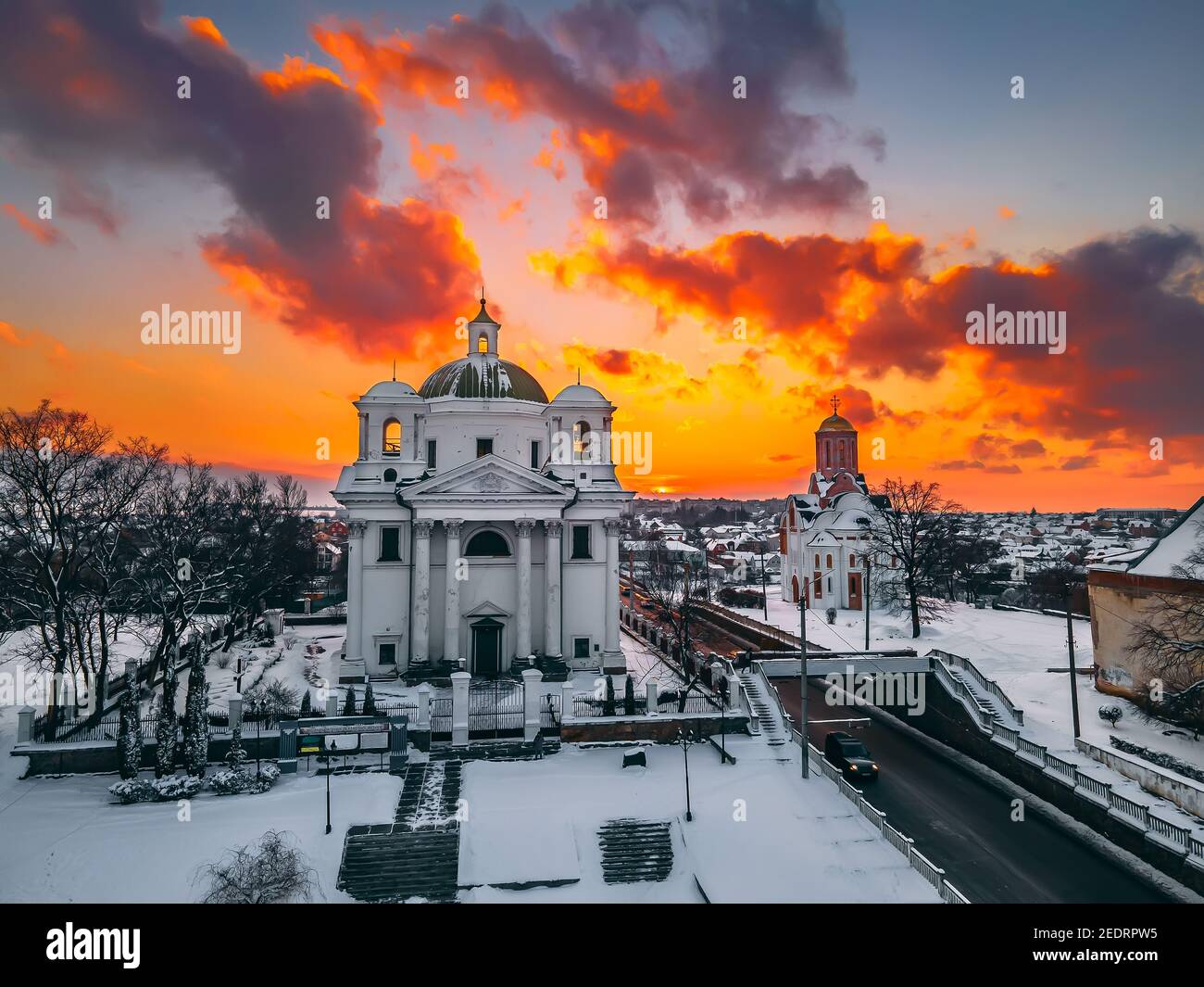 Vista aerea della cattedrale e della chiesa nella piccola città europea coperta di neve al luminoso tramonto d'inverno splendidi tramonti e nuvole. Drone. Inverno. Ukrain Foto Stock
