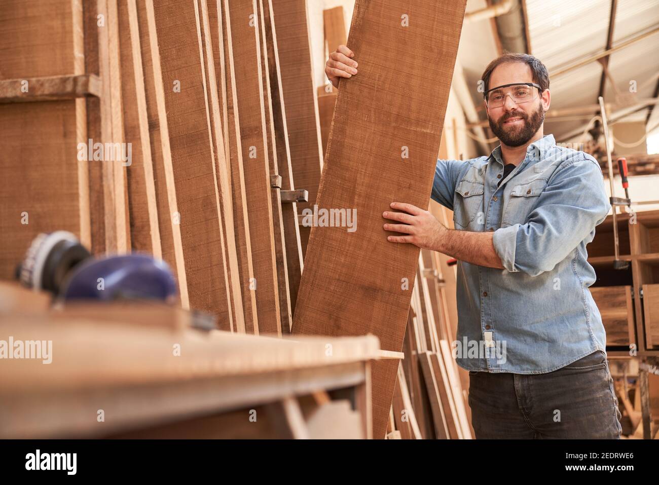 Falegname o falegname nel magazzino legno con un pezzo per la costruzione di mobili Foto Stock