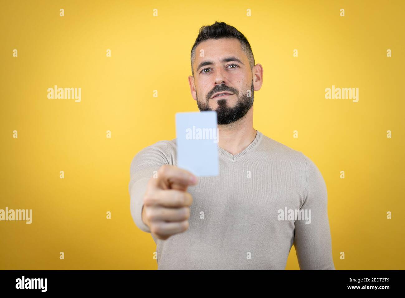 Bell'uomo con barba che indossa un pullover su sfondo giallo sorridente e tenendo la carta bianca Foto Stock