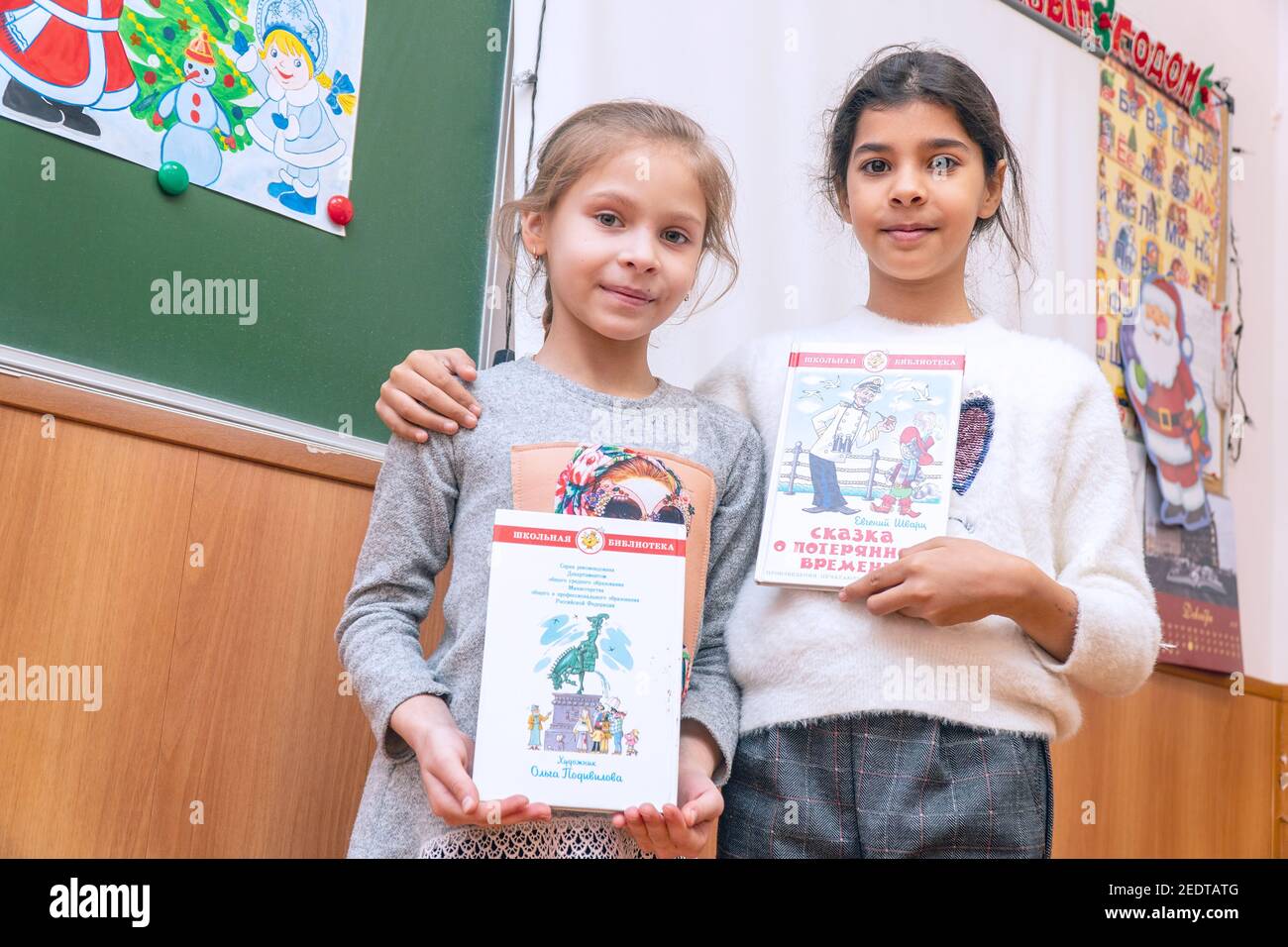 Chapaevsk, regione di Samara, Russia - 24 dicembre 2020: Due ragazze della scuola elementare stanno in classe al tabellone con i libri Foto Stock