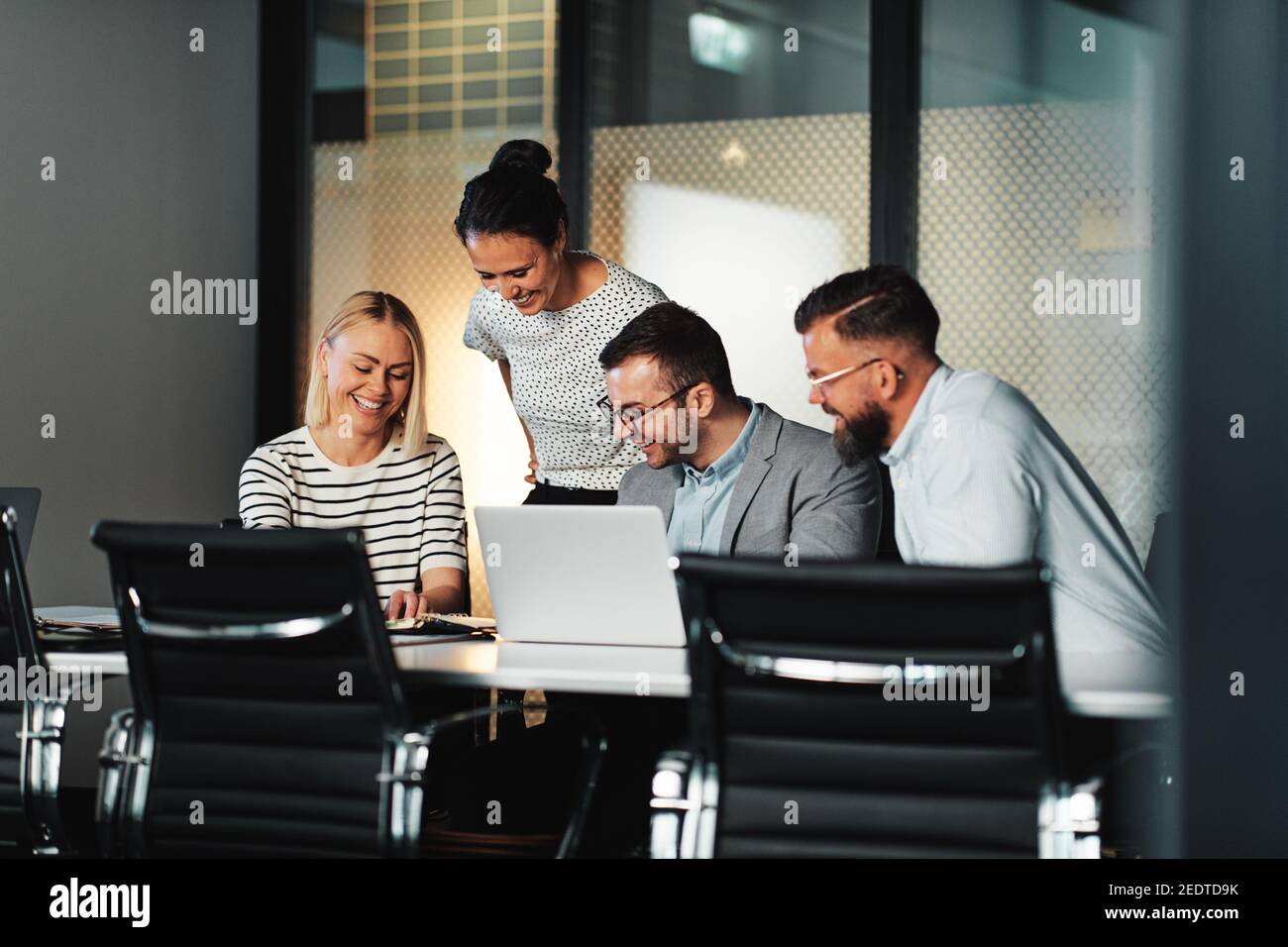 Gruppo di uomini d'affari sorridenti che lavorano su un computer portatile e discutono lavori di documentazione a un tavolo durante una riunione nella sala riunioni di un ufficio Foto Stock