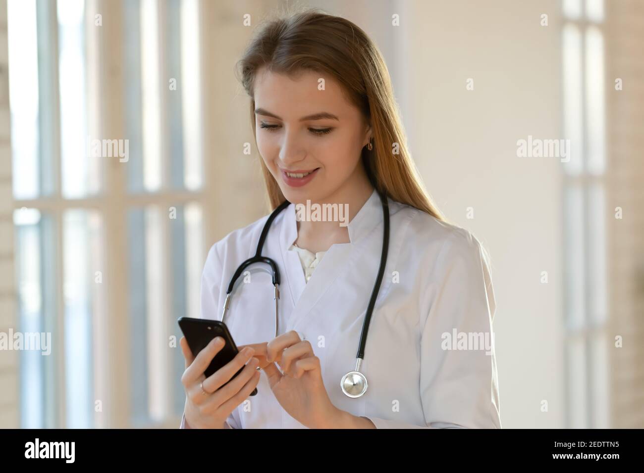 Sorridendo bello giovane medico generico utilizzando smartphone. Foto Stock