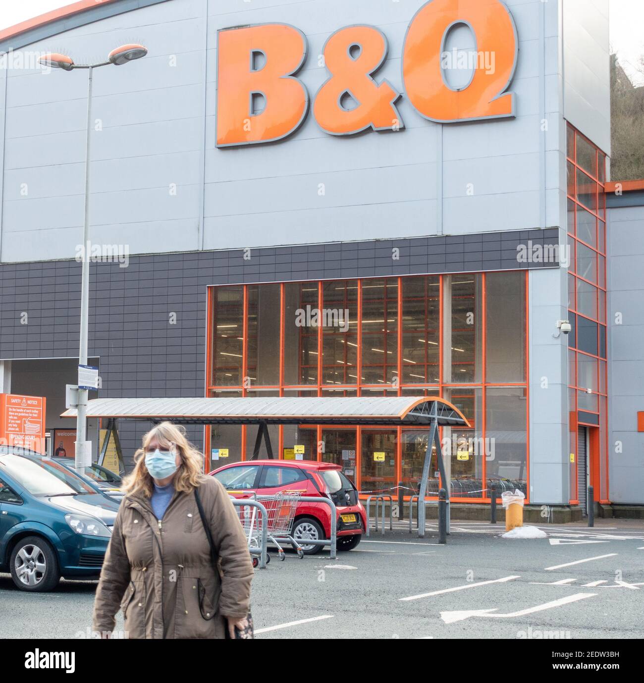 Una donna si allontana da un negozio di fai da te B&Q che indossa una copertura monouso per il viso durante il blocco della pandemia. Foto Stock