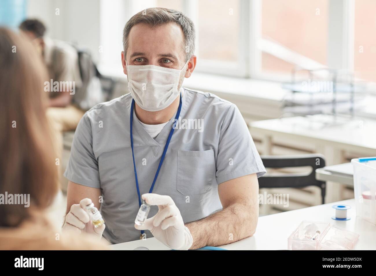 Ritratto del medico maschile maturo che indossa la maschera mentre si consulta il paziente prima della vaccinazione covid in clinica, copia spazio Foto Stock