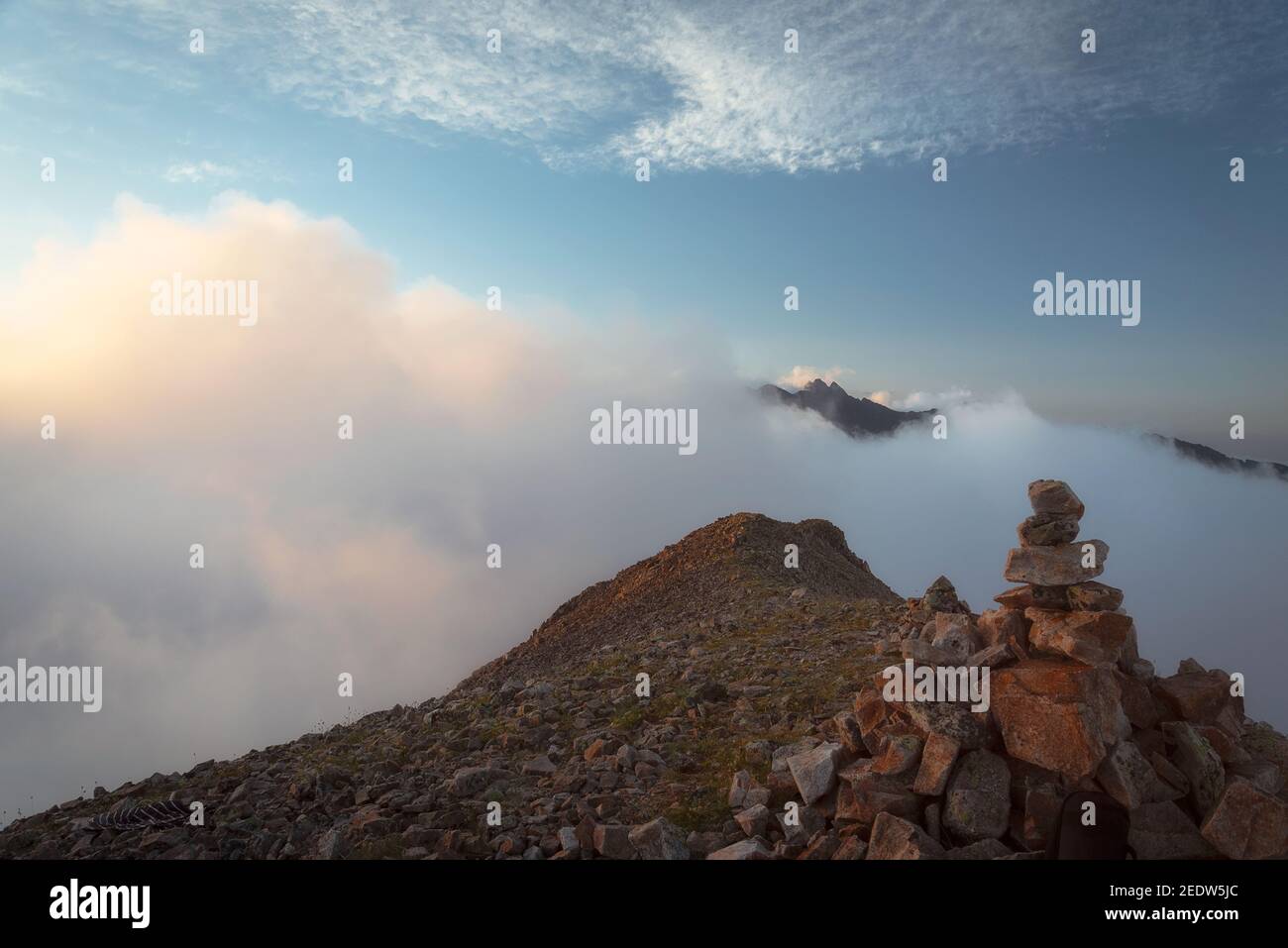 cairn sulla cima di una montagna circondata da nuvole con cielo serale Foto Stock