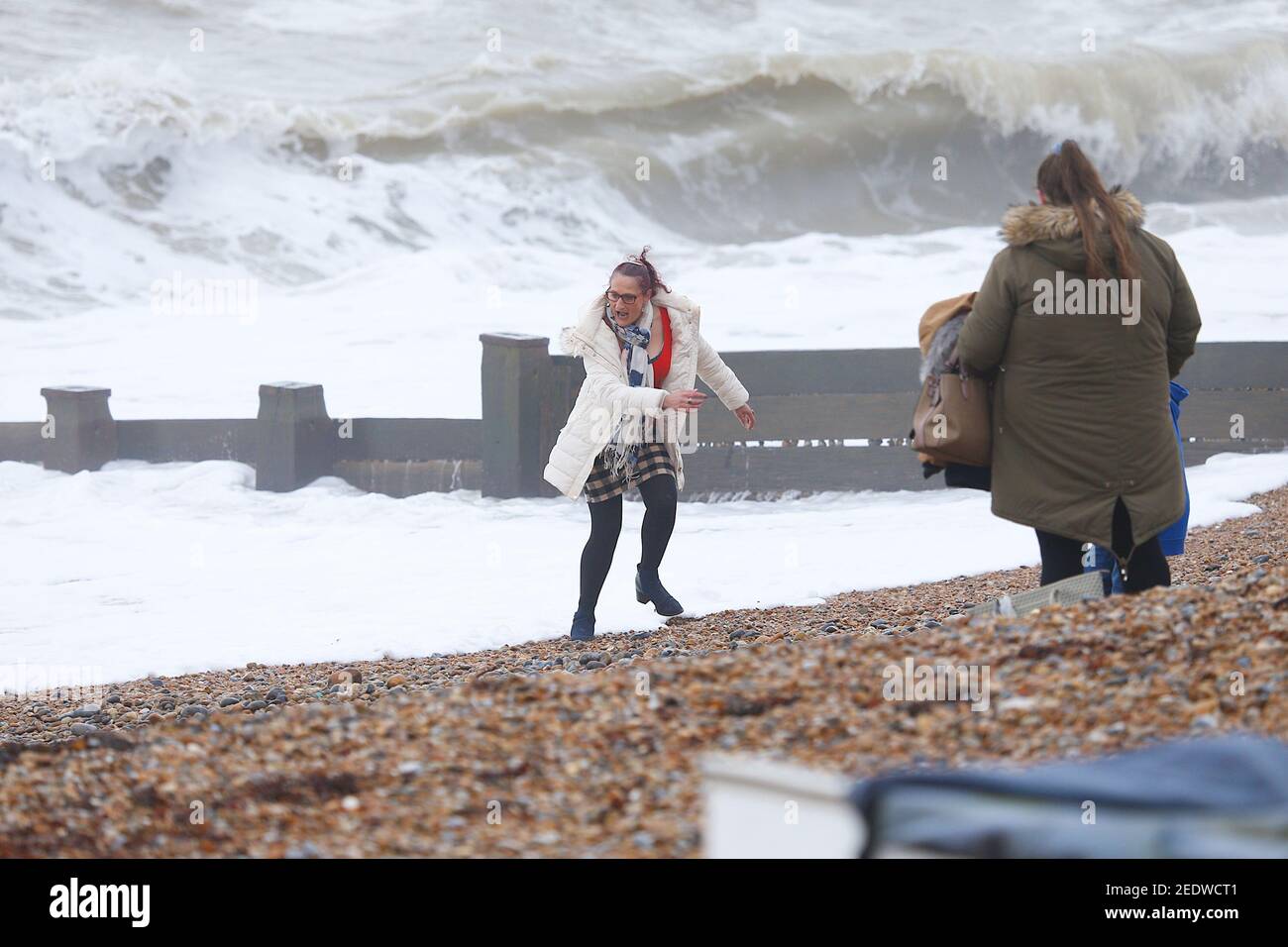 Bexhill-on-Sea, Sussex orientale, Regno Unito. 15 Feb 2021. UK Weather: Una giornata breezy e overcast a Bexhill con il tempo previsto per migliorare più tardi nella settimana. Una donna viene quasi catturata con un'onda. Photo Credit: Paul Lawrenson/Alamy Live News Foto Stock