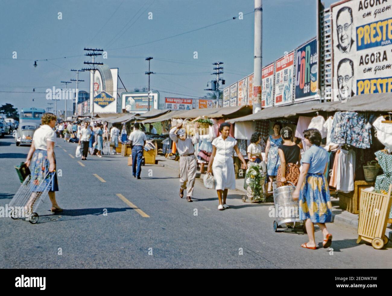 Un mercato di strada soleggiato e affollato che vende prodotti freschi e abbigliamento a São Paulo, Brasile 1961. Un poster (a destra) pubblicizza la campagna elettorale mayorale di Francisco Prestes Maia (1896–1965), l'architetto, ingegnere civile, urbanista e professore. Nel 1961, Prestes Maia è stato eletto e ha iniziato il suo terzo mandato come sindaco della città. São Paulo è una città del Brasile sud-orientale. São Paulo è la più grande città di lingua portoghese del mondo. Questa immagine proviene da una vecchia trasparenza di colore dilettante da 35 mm. Foto Stock