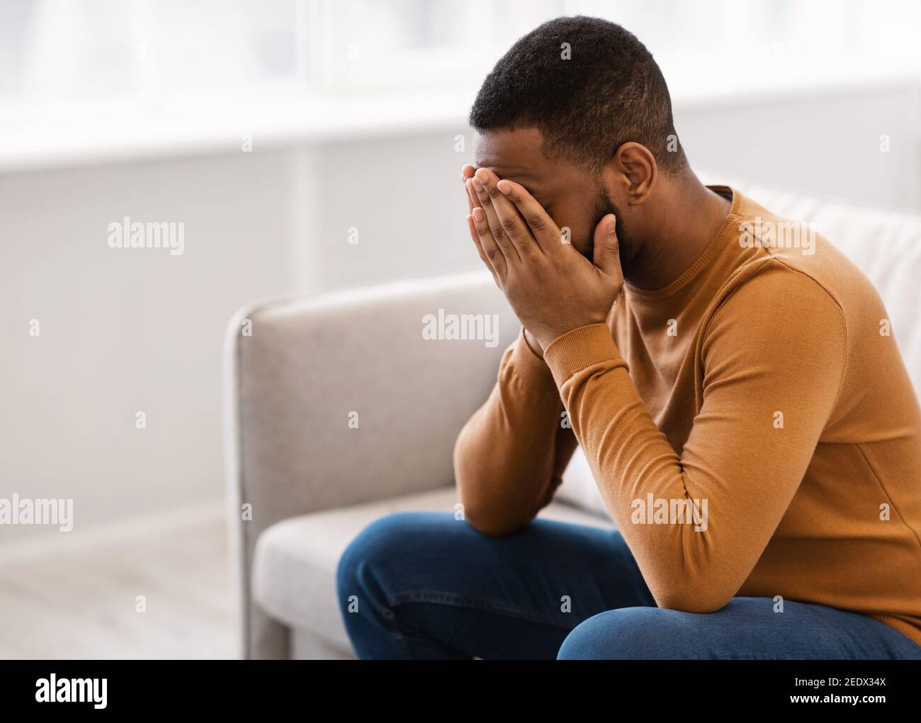 Desperate African Man copertura faccia piangendo avendo depressione a casa Foto Stock