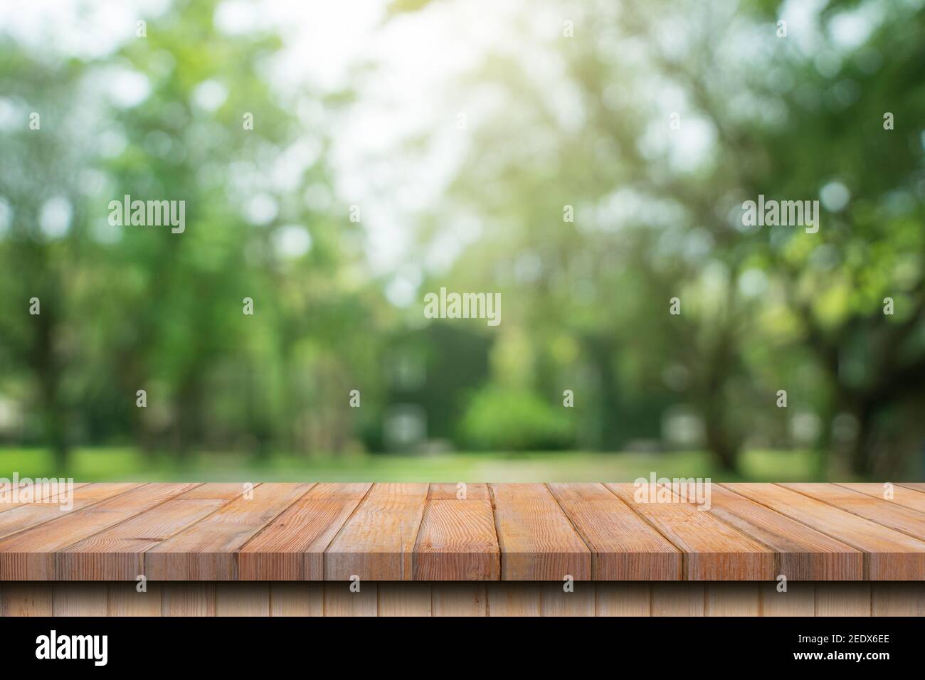 Tavolo vuoto in legno, bokeh sfocato e sfondo sfocato di alberi da giardino con luce solare. Modello di esposizione del prodotto. Foto Stock