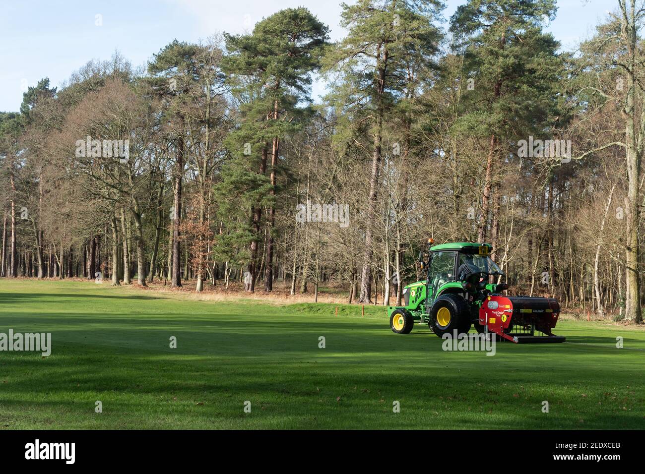 Groundsman falcia il verde con un trattore e un accessorio per falciatrice presso il golf club Aldershot Army, Hampshire, Regno Unito Foto Stock