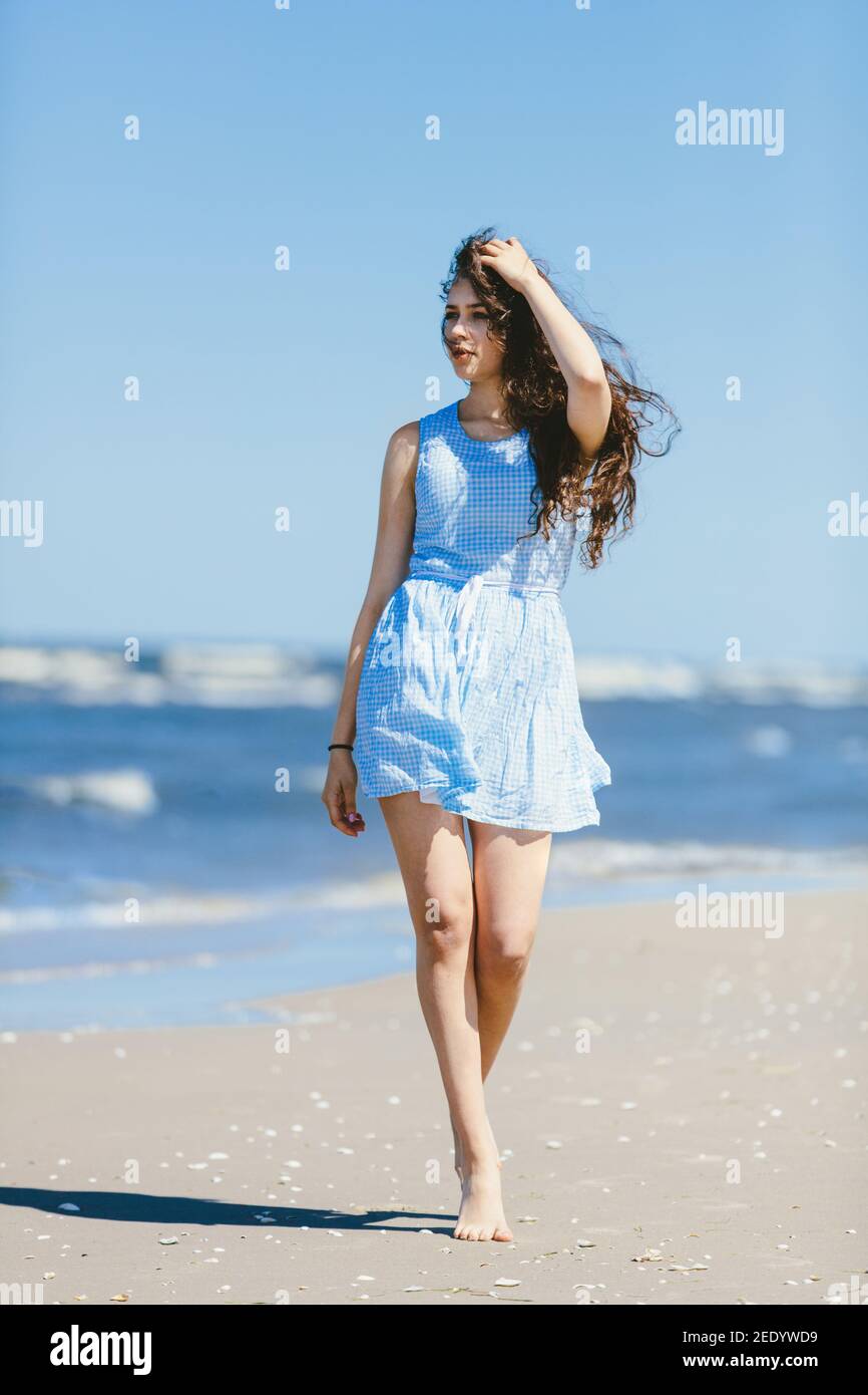 Giovane ragazza che cammina casualmente su una costa in un vestito blu. Estate al mare. Foto Stock