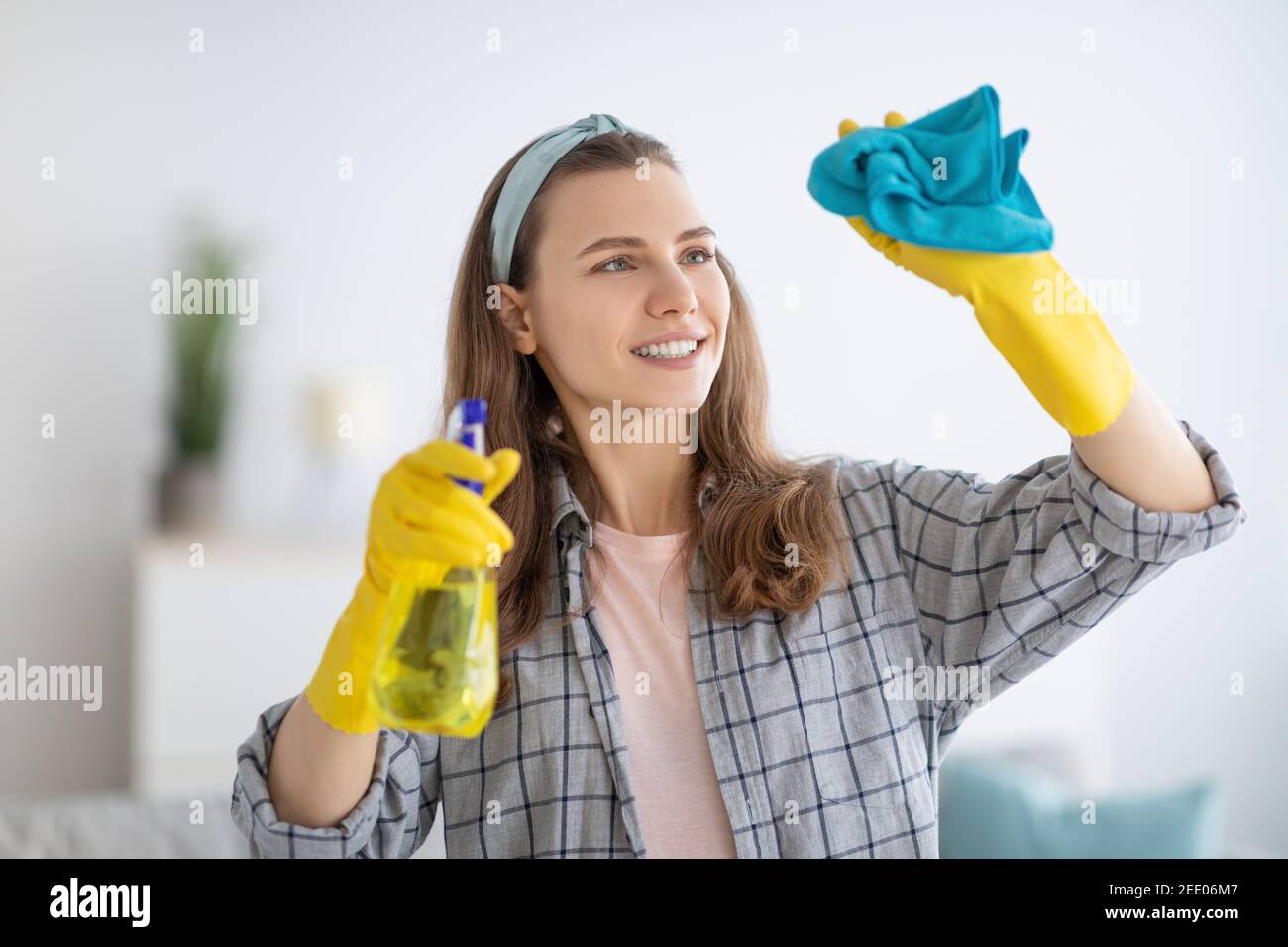 Bella donna millennial in guanti di gomma strofinando la finestra con spray detergente a casa Foto Stock