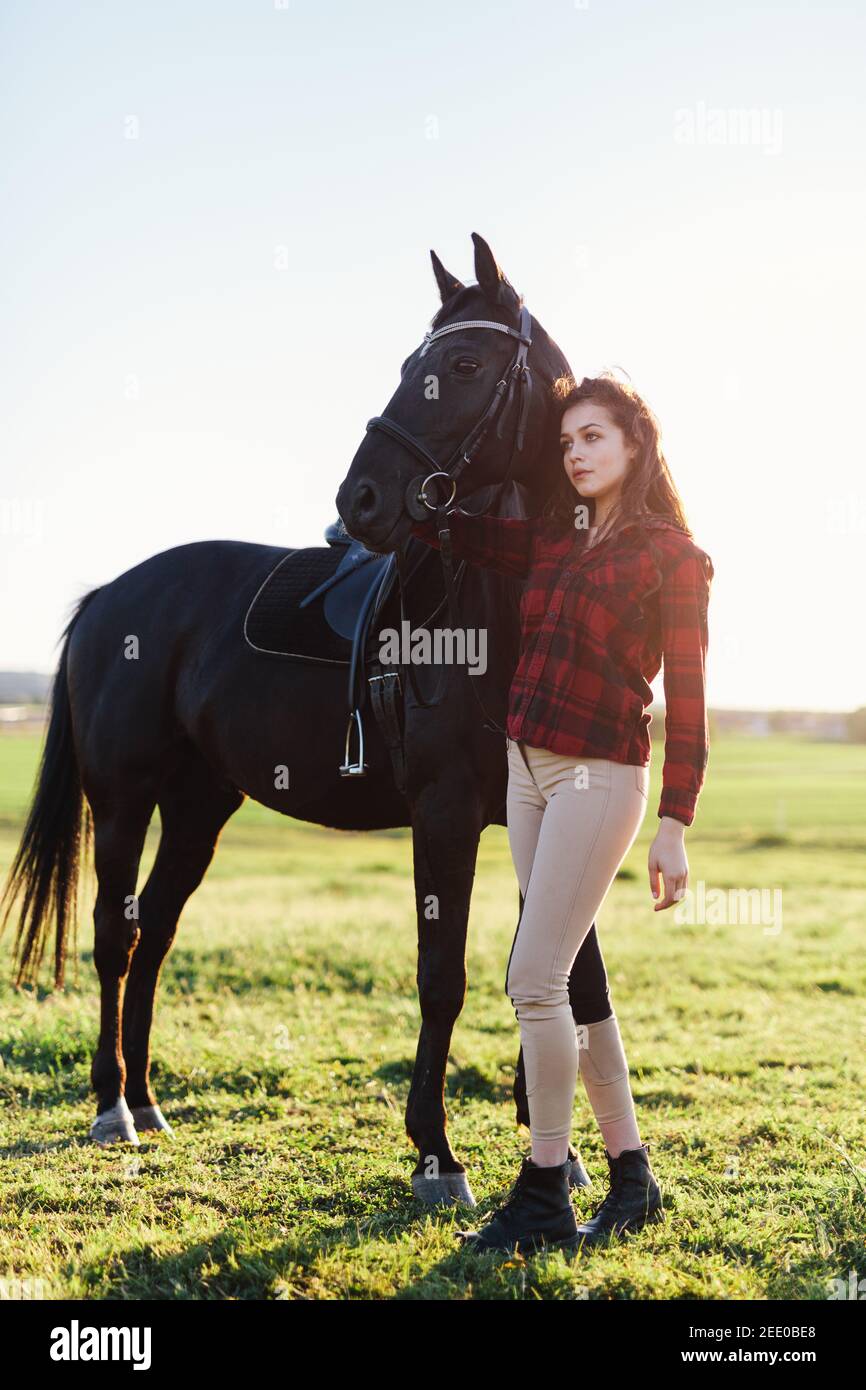 Cavallo nero e una giovane donna attraente in piedi accanto a lui. Amicizia umana e animale. Foto Stock