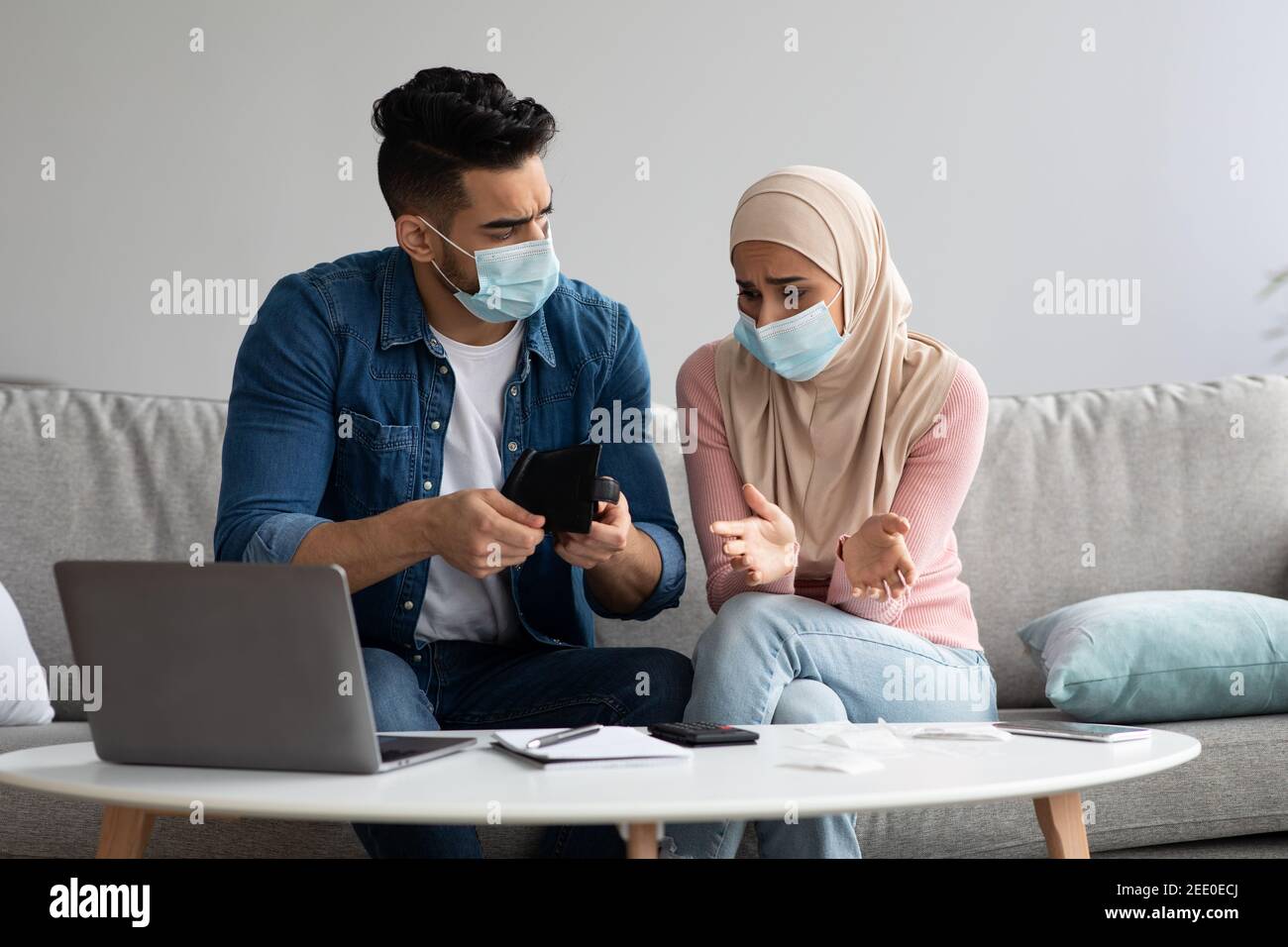 Coppia musulmana in maschere di faccia seduta sul divano, contando i soldi Foto Stock