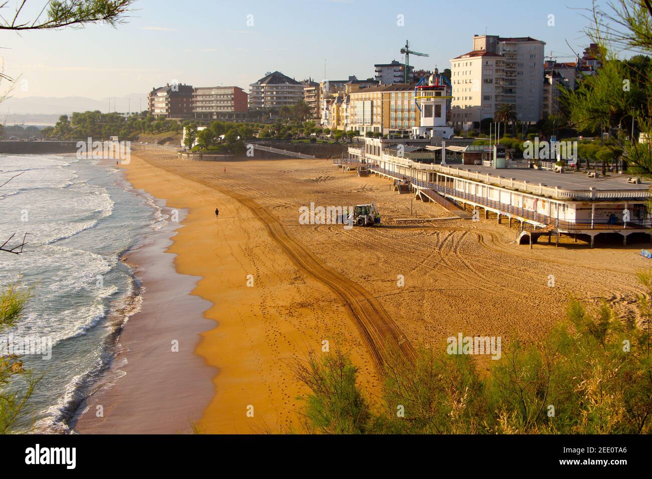 Un digger di pulizia spiaggia sulla spiaggia di Sardinero Santander Cantabria Spagna In una soleggiata mattina di primavera con il ristorante Maremmondo Foto Stock