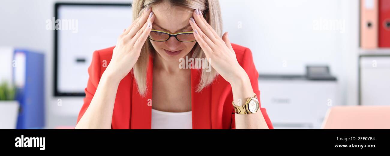 Donna stanca in tuta da lavoro che tiene la testa al computer portatile a tavola Foto Stock