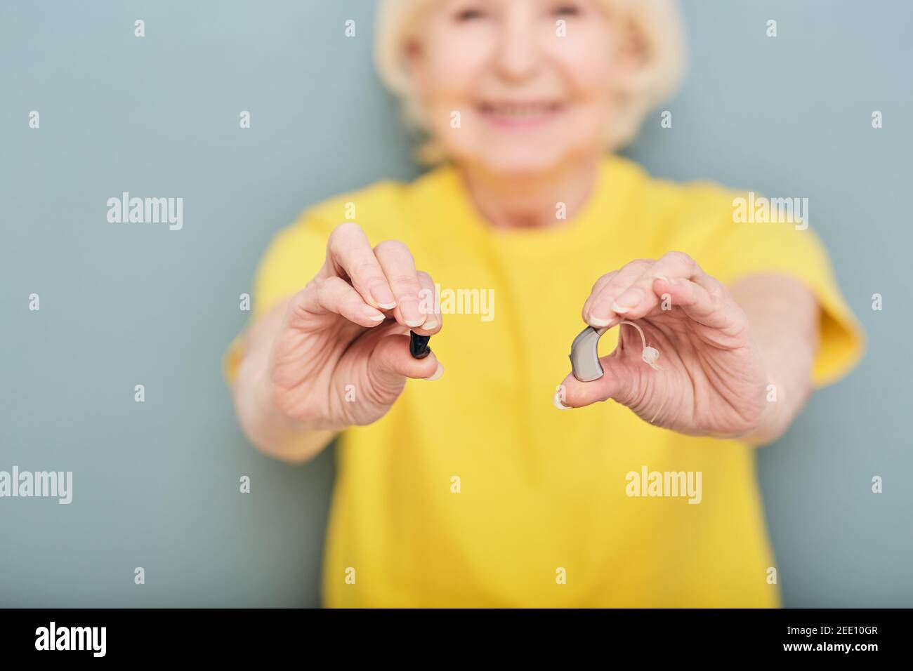 Vari apparecchi acustici per il trattamento della sordità per le persone anziane nelle mani delle donne anziane su sfondo grigio, messa a fuoco morbida Foto Stock