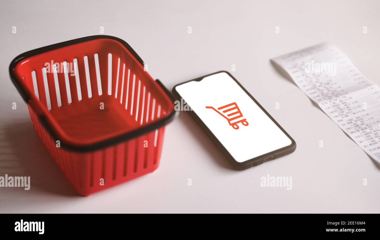 Smartphone accanto al cestino della spesa rosso e alla ricevuta della spesa. Online Store concetto di shopping e-commerce mockup Foto Stock