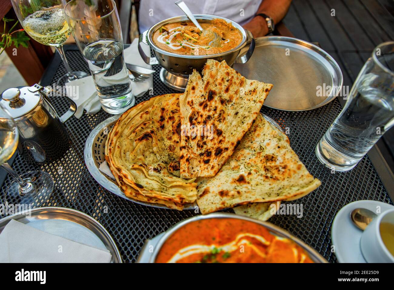 Tavola ricca di piatti indiani, pane (naan), bicchieri d'acqua, vino, caraffa con tè, ciotole e piatto. Ristorante indiano all'aperto. Foto Stock