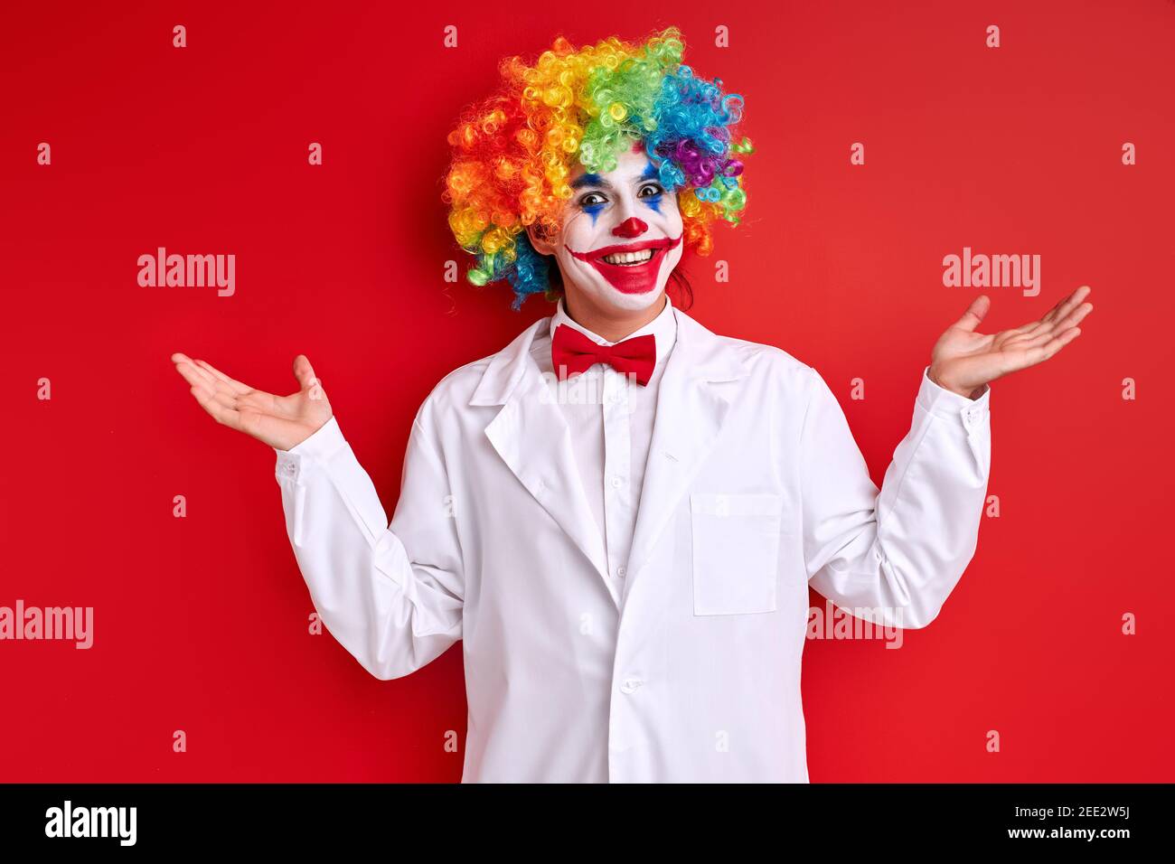 harlequin esecuzione, clown sorridente con volto felice indossando vestito bianco e volto dipinto su sfondo rosso Foto Stock