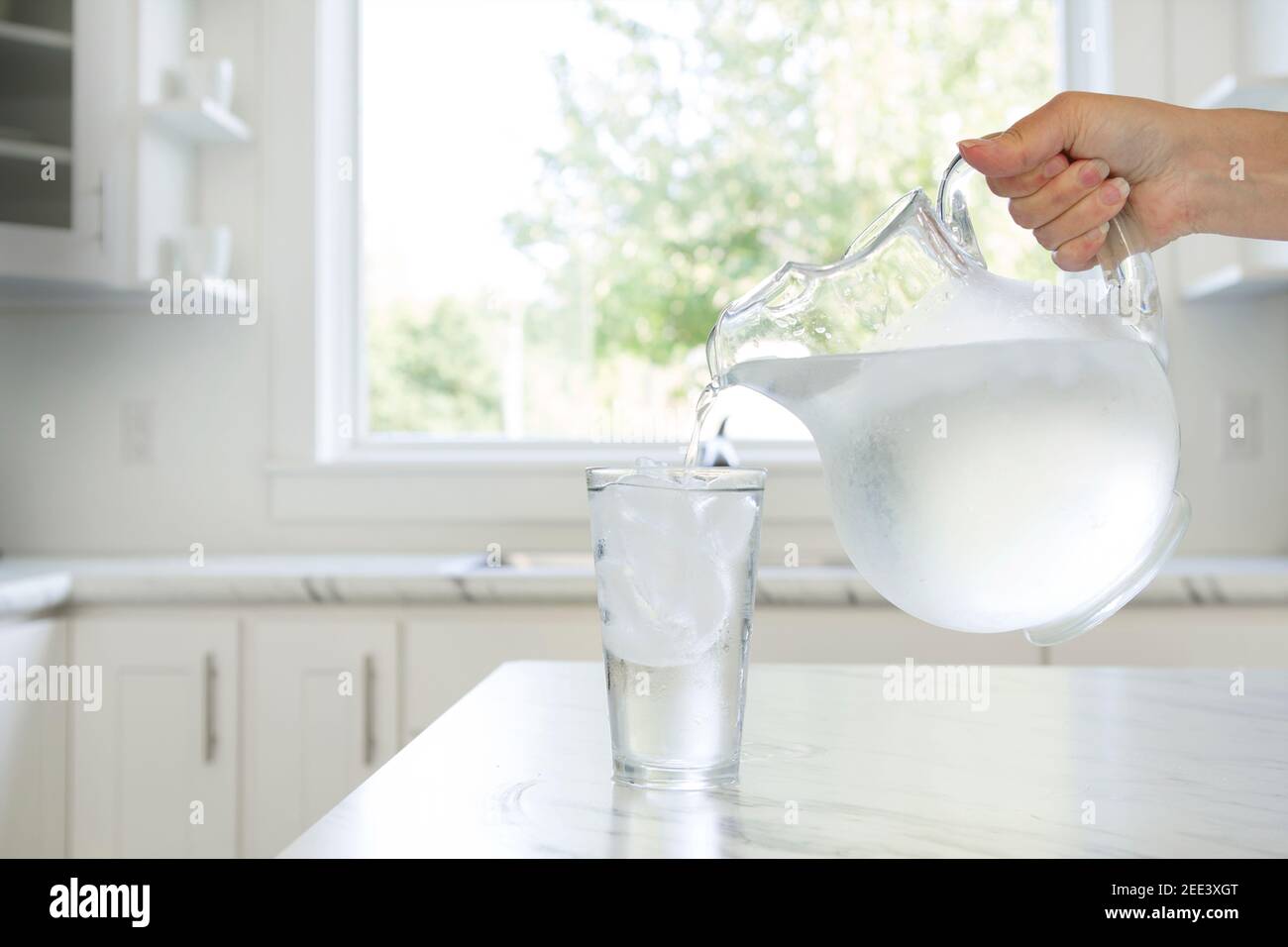 La mano di una donna che versa acqua ghiacciata da una caraffa in un bicchiere. Foto Stock